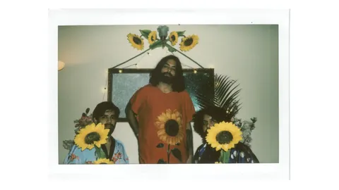Begum, the Delhi trio, in a faded instant photo, all three holding sunflowers under a sunflower garland