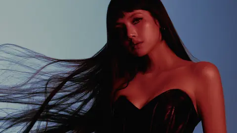 LISA in a black strapless top, long dark hair streaming sideways, lit red against a blue background